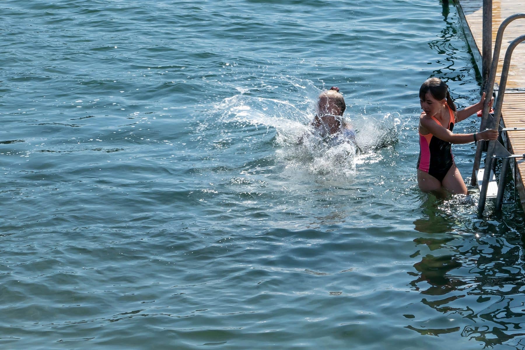 A child leaps into a calm sea from the rocks
