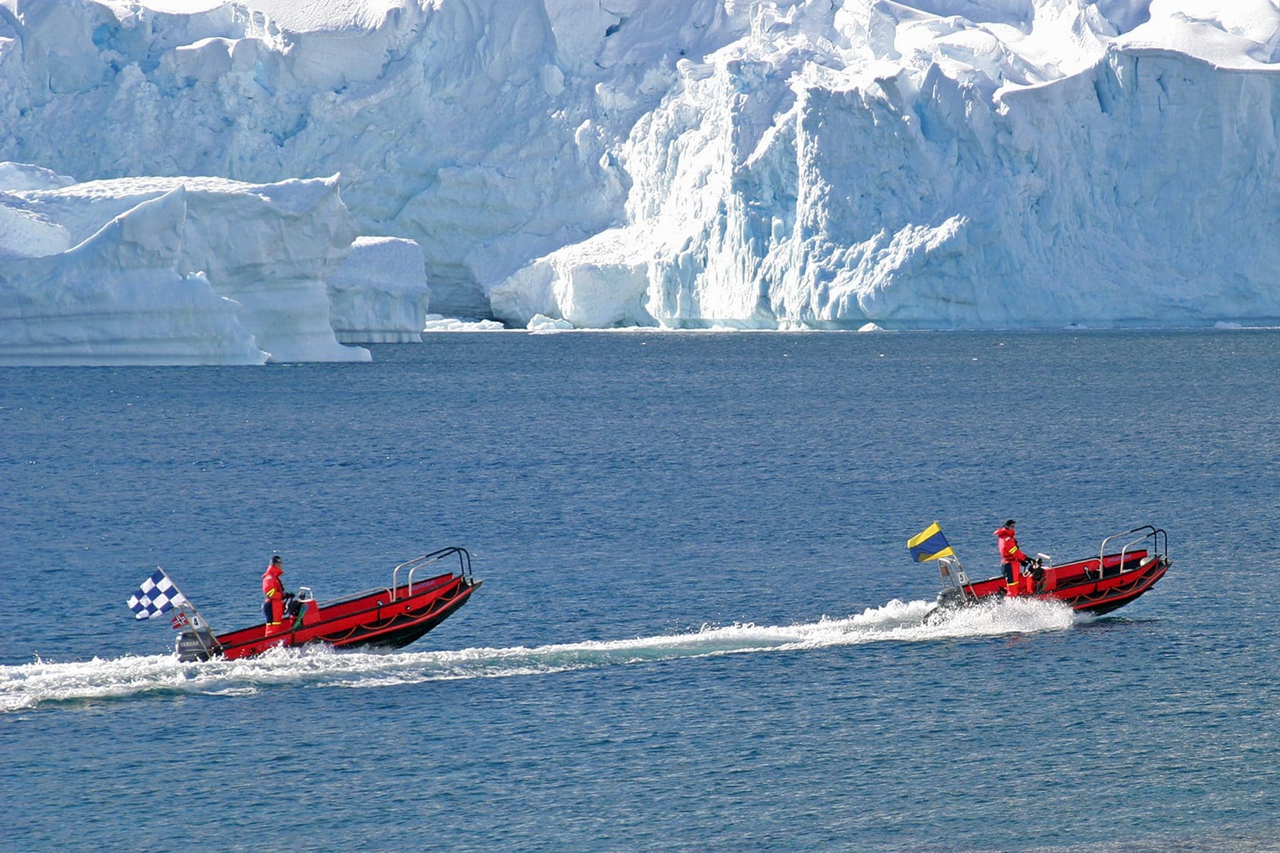 Two small expedition boats passing an ice-covered shore in the Lemaire Channel, Antarctica
