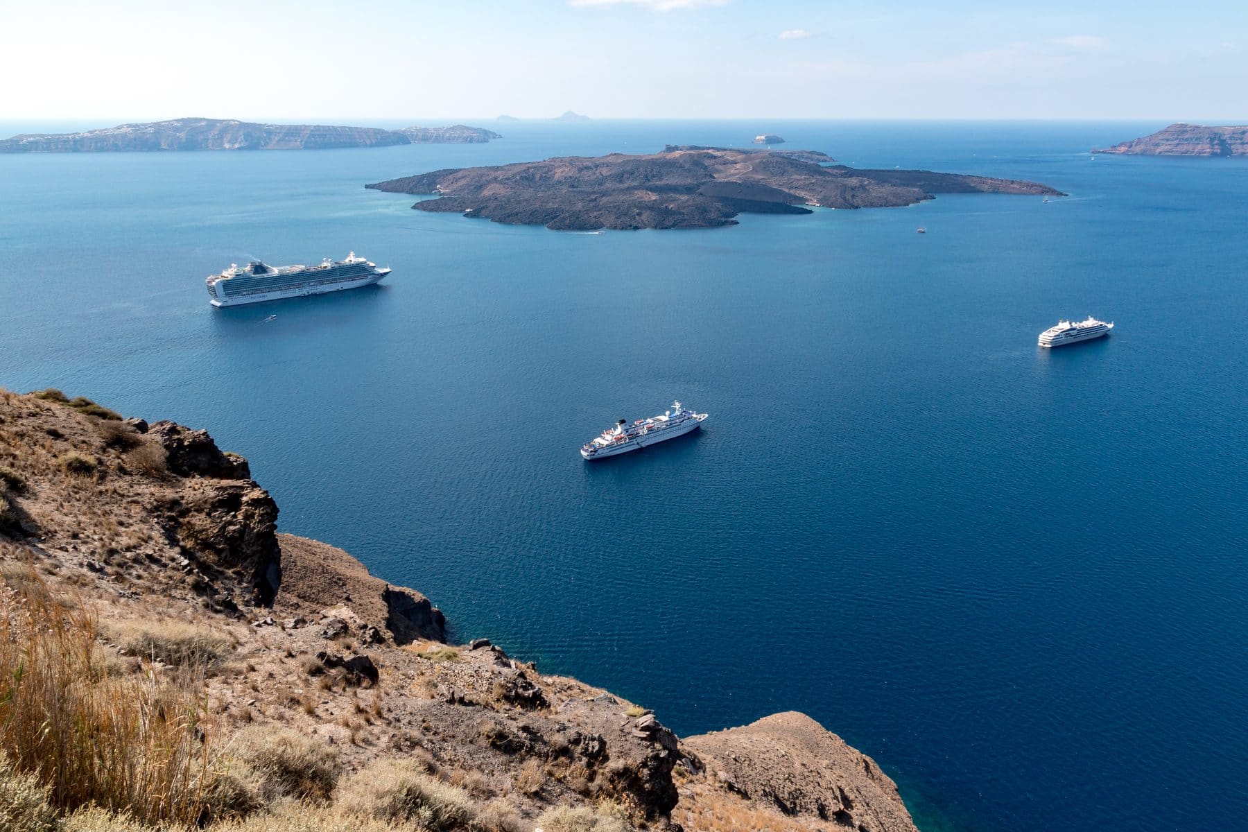 Cruise ships at anchor in the Santorini caldera below the volcanic island of Nea Kameni, seen from the cliffs of Fira