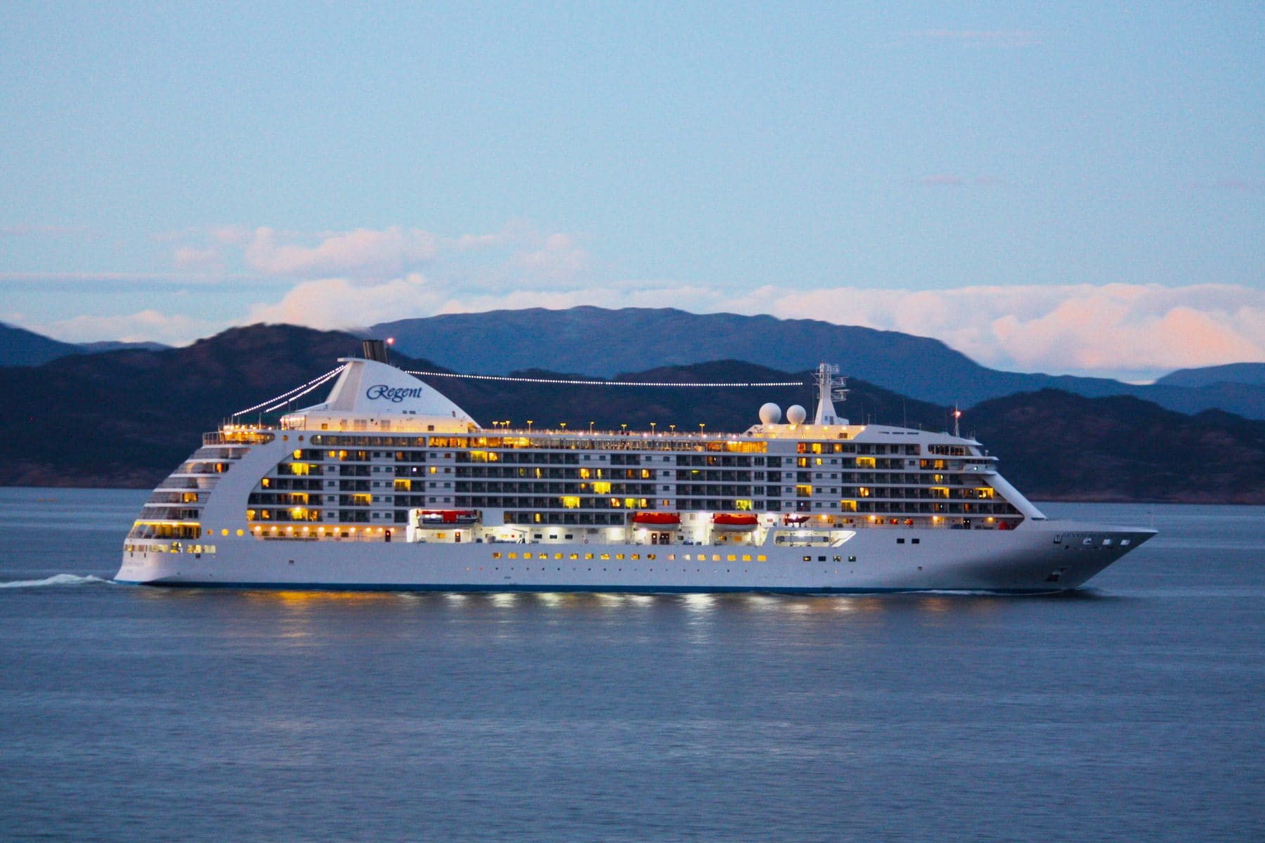 Seven Seas Voyager at dusk against a mountain shoreline