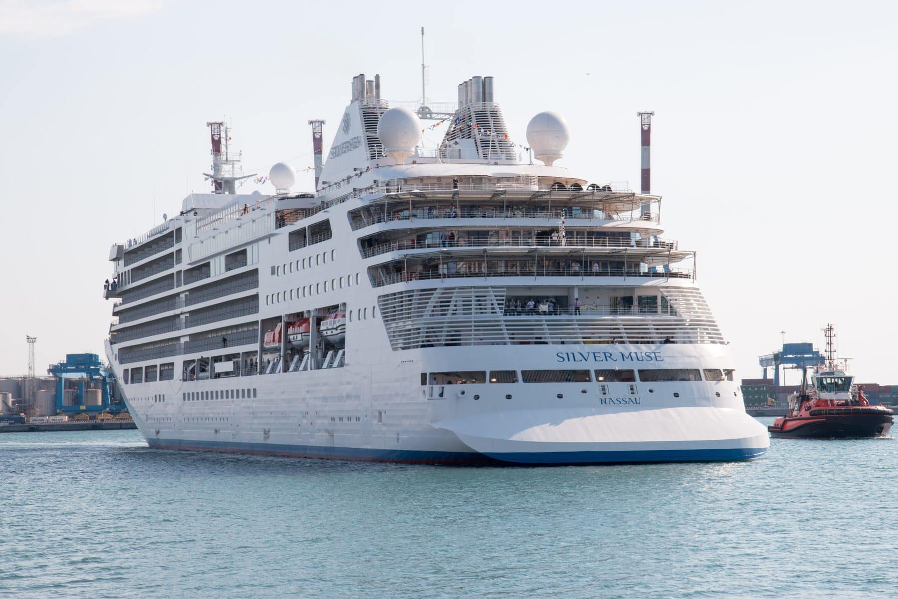 Silversea's Silver Muse under way off a container port, tugs alongside