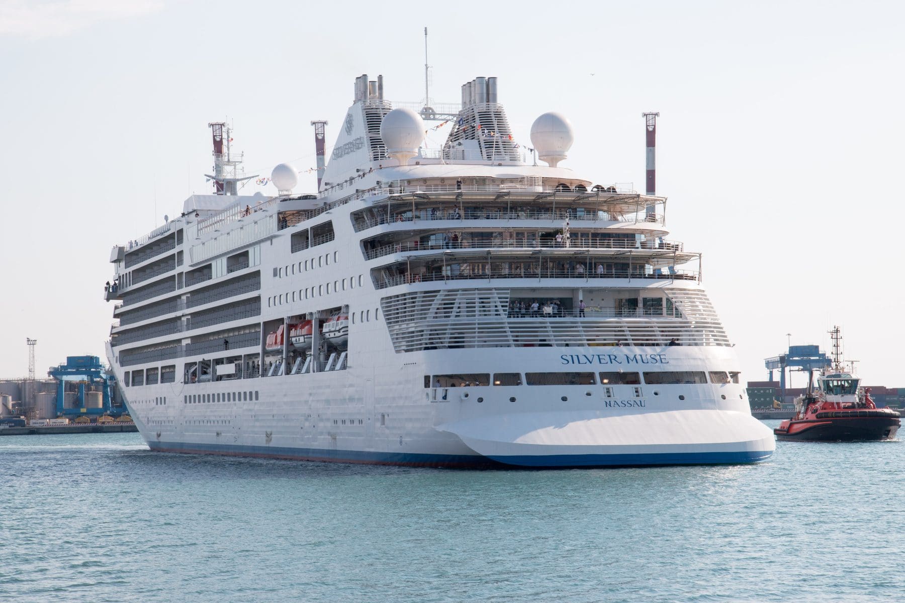 Silversea's Silver Muse under way off a container port, tugs alongside