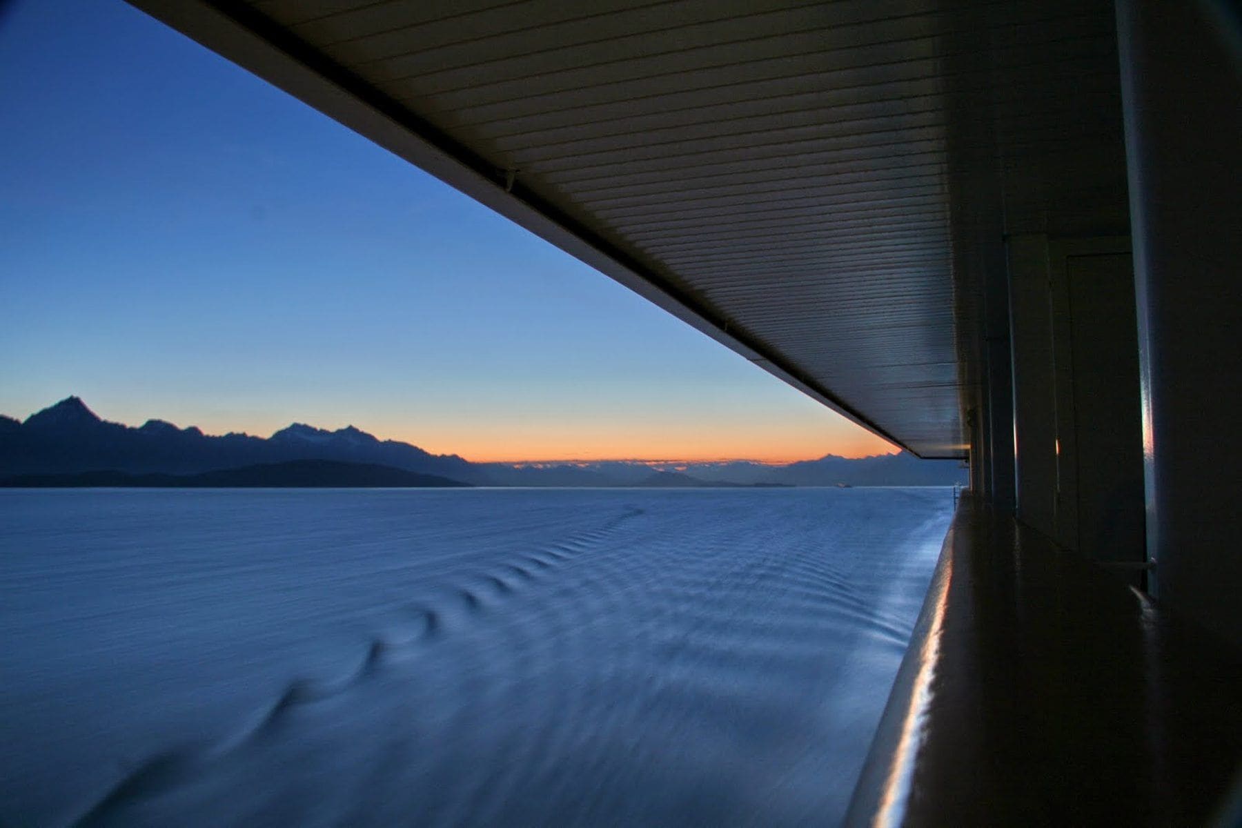 View from a ship's veranda at dusk as the wake curls past the mountains of Alaska's Inside Passage