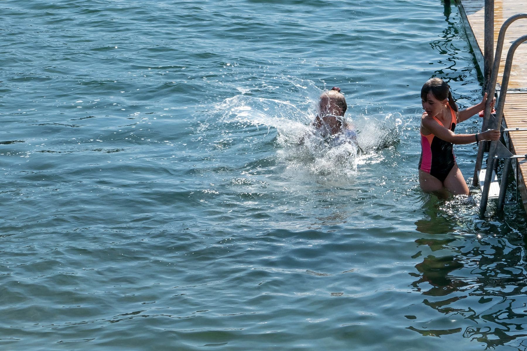 A child leaps into a calm sea from the rocks