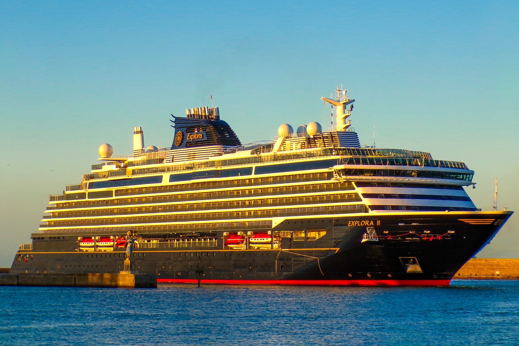 Explora II alongside in port in late-afternoon light, her dark hull and tiered decks catching the sun